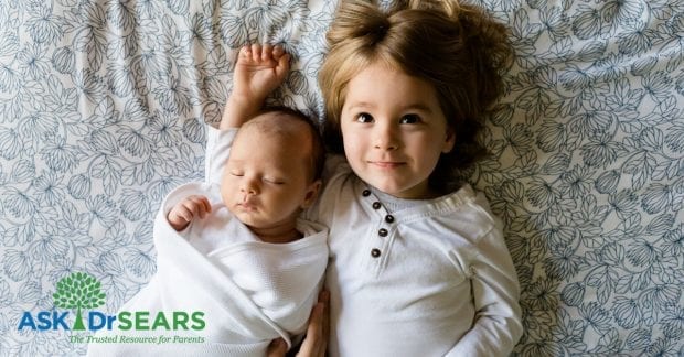 newborn and toddler siblings laying in bed together