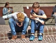 two teenage boys sitting on cell phones