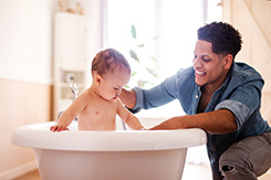 Baby in bathtub being bathed by smiling father.